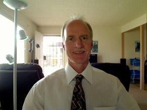 Man in white dress shirt and patterned tie smiling at camera in an office setting